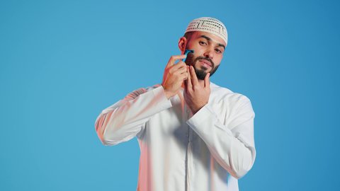 شفرة حلاقة رجالية، بورتريه  مقرب لرجل عربي خليجي اماراتي يرتدي الزي الاماراتي، يقوم بإزالة شعر الوجه بإستخدام شفرة الحلاقة ، مفهوم العناية بالبشرة والنظافة ، الإهتمام المظهر الخارجي ، خلفية ملونة