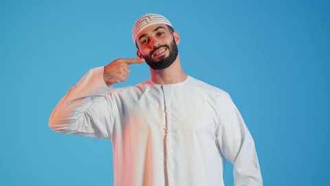 استخدام قشور فينير من الخزف للأسنان،تجميل وتبييض الاسنان،  بورتريه لرجل عربي اماراتي خليجي يبتسم ويشير بإصبعه السبابة على أسنانه، إبتسامة هوليود،  معالجة الأسنان، أسنان نظيفة مثالية ,خلفية ملونة