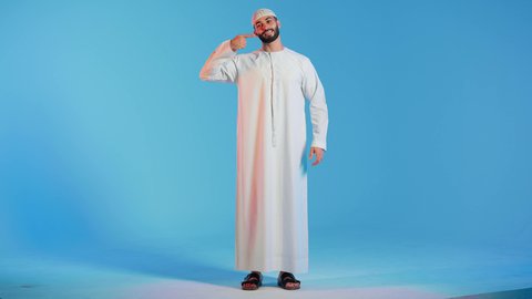 تجميل وتبييض الاسنان،  بورتريه لرجل عربي اماراتي خليجي يبتسم ويشير بإصبعه السبابة على أسنانه، إبتسامة هوليود،  معالجة الأسنان، أسنان نظيفة مثالية , استخدام قشور فينير من الخزف للأسنان،خلفية ملونة