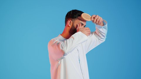 تعابير وإيماءات السعادة والسرور، ، مفهوم العناية والاهتمام بالجمال والأناقة والمظهر الخارجي،تمشيط وترتيب الشعر، بورتريه لرجل عربي خليجي اماراتي يقوم بتصفيف شعره باستخدام فرشاة الشعر ( المشط ) ، خلفية ملونة