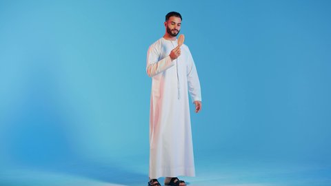 روتين العنايه اليومي ، تمشيط وترتيب الشعر، مفهوم الاهتمام بالجمال والأناقة والمظهر الخارجي، بورتريه لرجل عربي خليجي اماراتي يقوم بتصفيف شعره باستخدام فرشاة الشعر ( المشط ) بتعابير وإيماءات السعادة والسرور،، خلفية ملونة