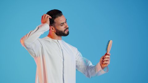 تمشيط وترتيب الشعر، مفهوم العناية والاهتمام بالجمال والأناقة والمظهر الخارجي، بورتريه لرجل عربي خليجي اماراتي يقوم بتصفيف شعره باستخدام فرشاة الشعر ( المشط ) بتعابير وإيماءات السعادة والسرور،، خلفية ملونة