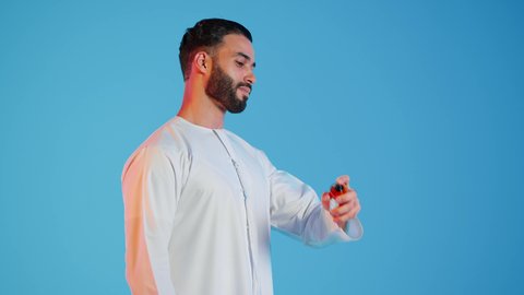 بورتريه مقرب لرجل عربي خليجي اماراتي يرتدي الزي الاماراتي، يقوم بوضع العطر،عطور ذات روائح فاخرة وفريدة، التسويق لمنتجات العطور، العود العطري، التطيب والتعطر  بالمناسبات والأعياد وحفلات الزفاف، ، مفهوم الأناقة والإهتمام المظهر الخارجي، خلفيه ملونه