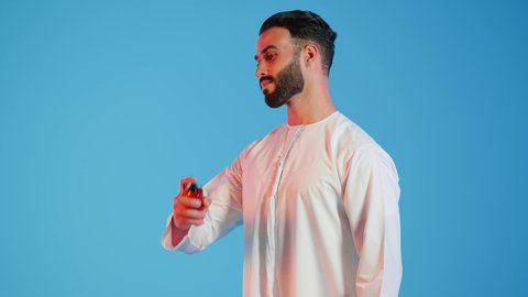التسويق لمنتجات العطور، العود العطري،عطور ذات روائح فاخرة وفريدة، بورتريه مقرب لرجل عربي خليجي اماراتي يرتدي الزي الاماراتي، يقوم بوضع العطر، التطيب والتعطر  بالمناسبات والأعياد وحفلات الزفاف، ، مفهوم الأناقة والإهتمام المظهر الخارجي، خلفيه ملونه