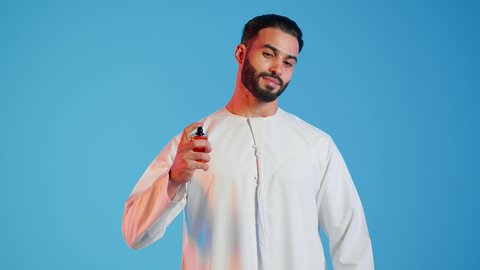 عطور ذات روائح فاخرة وفريدة، التسويق لمنتجات العطور، العود العطري، بورتريه مقرب لرجل عربي خليجي اماراتي يرتدي الزي الاماراتي، يقوم بوضع العطر، التطيب والتعطر  بالمناسبات والأعياد وحفلات الزفاف، ، مفهوم الأناقة والإهتمام المظهر الخارجي، خلفيه ملونه
