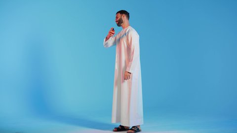 Perfumes with luxurious and unique scents, holiday and wedding occasions, marketing for perfume products, aromatic oud, a close-up portrait of an Emirati Gulf Arab man wearing traditional Emirati attire, applying perfume, the concept of elegance and attention to appearance, colorful background.