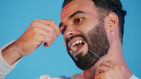 بورتريه مقرب لرجل عربي خليجي إماراتي مبتسم يقوم باستخدام خيط تنظيف الأسنان، مفهوم العناية والاهتمام بصحة ونظافة الفم والأسنان، روتين النظافة اليومية لتجنب تسوس الأسنان وأمراض اللثة، مفهوم العناية الشخصية، خلفية ملونة