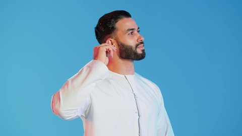 Using cotton swabs for cleaning, the concept of caring for and maintaining ear health and cleanliness, daily ear cleaning routine, a close-up portrait of an Emirati Gulf Arab man wearing traditional Emirati attire, cleaning his ear with a cotton swab, caring for ear cleanliness, colorful background.