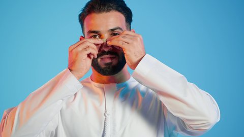 منتجات تجميلية فعالة وتقنيات حديثة ، تجربة فاخرة باستخدام ماسكات تنظيف المسام ، وعي الرجل العربي بأهمية العناية الشخصية، التخلص من الرؤوس السوداء والجلد الميت، مفهوم الاهتمام بنضارة وتحسين البشرة، بورتريه لرجل عربي خليجي اماراتي  يرتدي الزي التقليدي يضع لصقات الأنف ، خلفية ملونه .