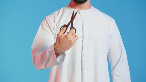 الاهتمام بالمظهر الخارجي والأناقة، عدم القدرة على التوقف من الكلام، مفهوم السكوت والصمت، بورتريه لرجل عربي خليجي اماراتي يرتدي الزي التقليدي يحمل بيده مقص ينظر الى الكاميرا بتعابير الجدية، الوقوف باستقامة وثبات،  خلفية ملونة