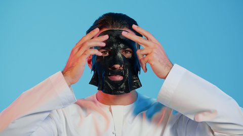 مفهوم العناية والاهتمام بالمظهر الخارجي، استخدام مكونات تجميلية، خطوات تنظيف وتقشير البشرة، بورتريه لرجل عربي خليجي اماراتي يرتدي الزي التقليدي يقوم بوضع قناع الطين على وجهه،  خلفية ملونة.