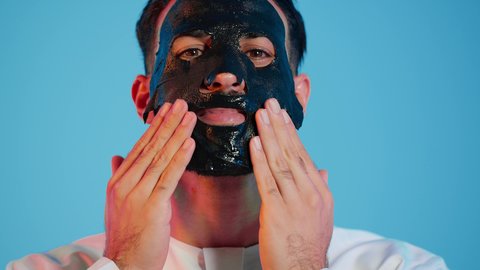 بورتريه لرجل عربي خليجي اماراتي يرتدي الزي التقليدي يقوم بوضع قناع الطين على وجهه، استخدام مكونات تجميلية، خطوات تنظيف وتقشير البشرة، مفهوم العناية والاهتمام بالمظهر الخارجي، خلفية ملونة.