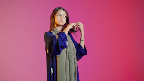 تعابير وإيماءات السعادة والسرور، مفهوم الانوثه والنعومه ، تمشيط وترتيب الشعر، مفهوم العناية والاهتمام بالجمال والأناقة والمظهر الخارجي، بورتريه لامراه عربيه خليجيه اماراتيه تقوم بتصفيف شعرها باستخدام فرشاة الشعر ( المشط ) ، خلفية ملونة