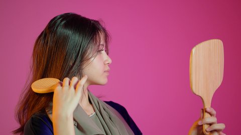 The concept of femininity and softness, combing and arranging hair, the concept of care and attention to beauty, elegance, and appearance, a portrait of an Arab Gulf Emirati woman styling her hair using a hairbrush (comb) with expressions and gestures of happiness and joy, colorful background.