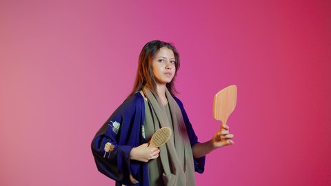 مفهوم العناية والاهتمام بالجمال والأناقة والمظهر الخارجي، مفهوم الانوثه والنعومه ، تمشيط وترتيب الشعر، بورتريه لامراه عربيه خليجيه اماراتيه تقوم بتصفيف شعرها باستخدام فرشاة الشعر ( المشط ) بتعابير وإيماءات السعادة والسرور،، خلفية ملونة