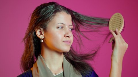 The concept of femininity and softness, combing and arranging hair, the concept of care and attention to beauty, elegance, and appearance, a portrait of an Arab Gulf Emirati woman styling her hair using a hairbrush (comb) with expressions and gestures of happiness and joy, colorful background.