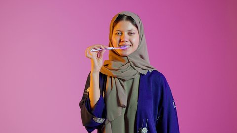تجنب تسوس الاسنان وامراض اللثة ،بورتريه مقرب لسيدة عربية خليجية اماراتيه  تقوم بتنظيف الأسنان بفرشاة الأسنان ، مفهوم العناية والإهتمام بصحة ونظافة الأسنان ، روتين نظافة الفم اليومية ، خلفية ملونة