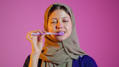 روتين نظافة الفم اليومية ،بورتريه مقرب لسيدة عربية خليجية اماراتيه  تقوم بتنظيف الأسنان بفرشاة الأسنان ، مفهوم العناية والإهتمام بصحة ونظافة الأسنان ،  تجنب تسوس الاسنان وامراض اللثة ، خلفية ملونة