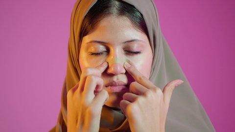 العناية بنضارة وتحسين البشرة،التخلص من الرؤوس السوداء والجلد الميت،  استخدام ماسك تنظيف المسام ومكون تجميلي، بورتريه مقرب لامرأة عربية خليجية اماراتيه  ترتدي العباءة والحجاب تضع لصاقة الأنف، مفهوم الاهتمام بالمظهر الخارجي للنساء، خلفية ملونة