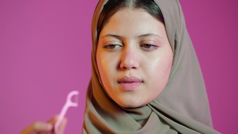 بورتريه لامراه عربية خليجيه اماراتيه ترتدي العباءة والحجاب  ، تقوم بإستخدام خيط تنظيف الأسنان ، مفهوم العناية والإهتمام بصحة الأسنان ، معدات طب الأسنان ، نظافة الأسنان يوميا ، خلفية ملونه