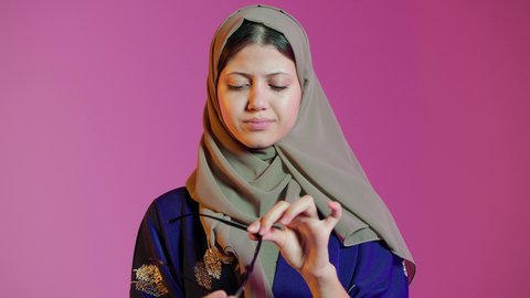 مفهوم ضعف النظر، ماركات عالمية فاخرة، تحسين وتصحيح الرؤية، بورتريه مقرب لسيدة عربية خليجية اماراتيه ترتدي العباءة والحجاب  تقوم باختيار نظارة ملائمة لملامح الوجه،  الاعجاب بالنظارات الطبية الجديدة، خلفية ملونة