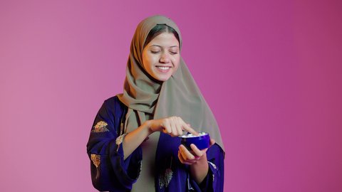 مفهوم العناية بنضارة وتحسين البشرة، الاهتمام بالمظهر الخارجي، بورتريه مقرب لامرأة عربية خليجية اماراتيه محجبة مبتسمة تضع كريم الترطيب، استخدام كريمات ومكونات تجميلية، خلفية ملونة