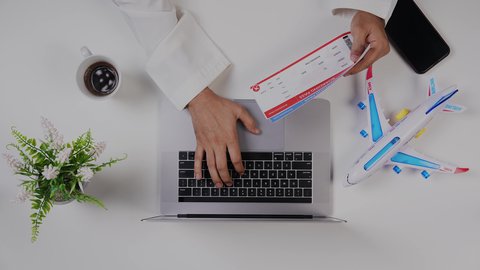 تصوير مقرب من الأعلى لرجل خليجي سعودي يضع معلومات تذاكر الرحلات الى اللابتوب في المطار , بيئة عمل مكتبية , خلفية بيضاء .