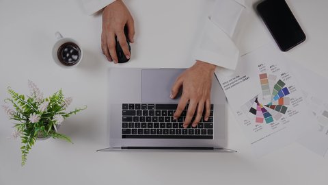 مصمم خليجي يعمل من خلال اللابتوب على مكتب أبيض, وظيفة ومهن سعودية,استخدام التقنيات الحديثة ،  تصوير مقرب من الأعلى لرجل سعودي عربي لديه خبره بدرجات الألوان ,بيئة عمل  مكتبية, خلفية بيضاء .