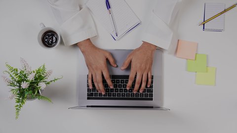 تصوير مقرب من الأعلى ليد ولد  سعودي عربي يعمل من خلال اللابتوب على مكتب أبيض , الاستمتاع بالمشروبات الساخنه ،مهن ووظيفة سعودية , بيئة عمل مكتبية , خلفية بيضاء .