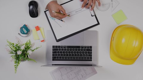 تدوين الملاحظات الهامة ، تصوير مقرب من الأعلى  لمهندس معماري خليجي , مهندس يعمل على تصميم العمارات من خلال اللابتوب على مكتب أبيض , وظيفه ومهن سعودية , بيئة عمل مكتبية , خلفية بيضاء .