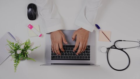 دمج التكنولوجيا بالطب،مفهوم الرعاية الصحية ، القطاع الطبي بالمملكة العربية السعودية, تصوير مقرب من الأعلى لطبيب خليجي سعودي يعمل على الحاسوب المحمول في العيادة, تقديم الاستشارات الطبية