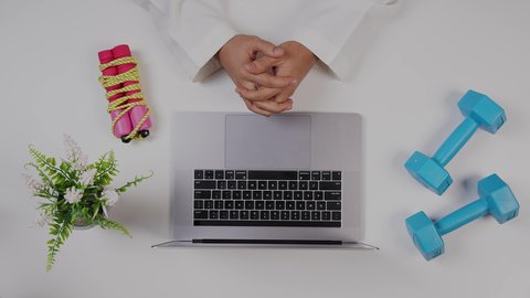 مهنة ووظيفه سعودية , الاهتمام باللياقة البدنية ،تصوير  مقرب من الأعلى لمدرب رياضي يعمل من خلال اللابتوب على مكتب أبيض ,بيئة عمل مكتبية ، خلفية بيضاء .