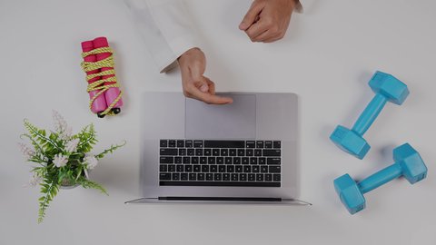 الاهتمام باللياقة البدنية ،تصوير  مقرب من الأعلى لمدرب رياضي يعمل من خلال اللابتوب على مكتب أبيض , مهنة ووظيفه سعودية , بيئة عمل مكتبية ، خلفية بيضاء .