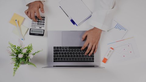 تصوير مقرب من الأعلى  لرجل عربي سعودي لديه خبره بالمحاسبة  , يعمل من خلال اللابتوب على مكتب أبيض , وظيفه ومهن سعودية , بيئة عمل مكتبية, خلفية بيضاء .