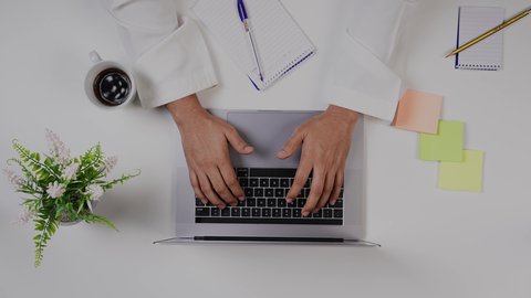 تصوير مقرب من الأعلى  ليد ولد سعودي عربي يعمل من خلال اللابتوب على مكتب أبيض , مهن ووظيفة سعودية , بيئة عمل مكتبية , خلفية بيضاء .