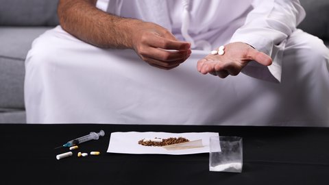 المخاطر الاجتماعية والصحية للإدمان، تعاطي المواد السامة، القيام بعادات سلوكية ضارة، المعاناة من الاضطرابات النفسية والمشاكل الصحية، صورة مقربة لأيدي رجل عربي خليجي إماراتي يحمل مجموعة من الحبوب مخدرة