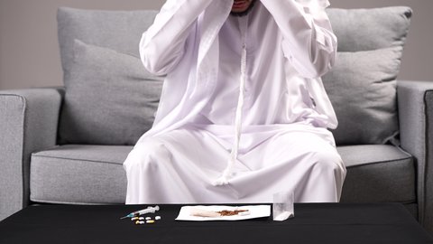 الإحساس بالوجع في الرأس، تصوير مقرب لرجل عربي خليجي إماراتي يرتدي الكندورة والغترة يضع يده على رأسه بإيماءات التعب والإرهاق، تعابير الضجر والاكتئاب عند إيقاف التدخين، الأعراض الجانبية لسحب المواد المخدرة من الجسم