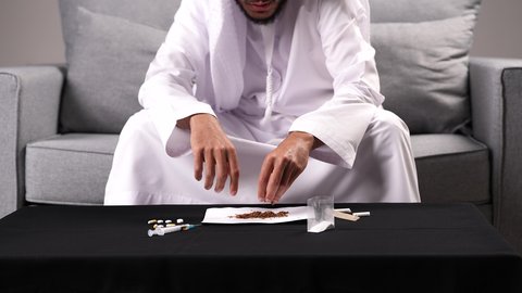سلوكيات ضارة وتأثير تعاطي المواد السامة على الصحة، الأثار السلبية للادمان على التبغ والمخدرات، المعاناة من الاضطرابات النفسية والمشاكل الصحية، تصوير مقرب لرجل عربي خليجي إماراتي يرتدي الكندورة يقوم بحشو عقب السجائر