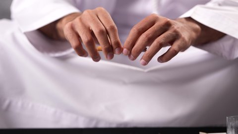 عادات وسلوكيات ضارة تؤدي إلى تعاطي المواد السامة، الأثار السلبية للادمان على التبغ والمخدرات، المعاناة من الاضطرابات النفسية والمشاكل الصحية، تصوير مقرب لرجل عربي خليجي إماراتي يرتدي الكندورة يقوم بحشو عقب السجائر