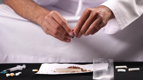 الأثار السلبية للادمان على التبغ والمخدرات، القيام بعادات سلوكية ضارة وتعاطي المواد السامة، المعاناة من الاضطرابات النفسية والمشاكل الصحية، تصوير مقرب لرجل عربي خليجي إماراتي يرتدي الكندورة يقوم بحشو عقب السجائر