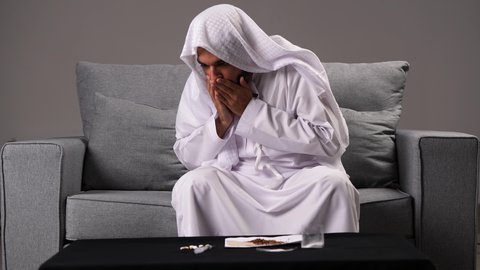الأعراض الجانبية لسحب المواد المخدرة من الجسم، الإحساس بالصداع والمعاناة من آلام الرأس، تصوير مقرب لرجل عربي خليجي إماراتي يرتدي الكندورة والغترة يضع يده على رأسه بإيماءات التعب والإرهاق، تعابير الضجر والاكتئاب عند إيقاف التدخين