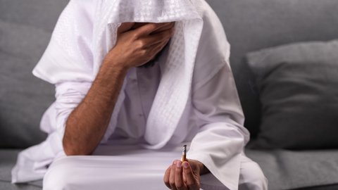 عادات سلوكية ضارة وتعاطي مواد سامة، المعاناة من الاضطرابات النفسية والمشاكل الصحية، الادمان على التبغ والمخدرات، معاقبة النفس وتأنيب الضمير، رجل عربي خليجي إماراتي يرتدي الكندورة يمسك بيدية سيجارة حشيش