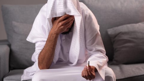 المعاناة من الاضطرابات النفسية والمشاكل الصحية، الادمان على التبغ والمخدرات، معاقبة النفس وتأنيب الضمير، رجل عربي خليجي إماراتي يرتدي الكندورة يمسك بيدية سيجارة حشيش، عادات سلوكية ضارة وتعاطي مواد سامة