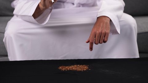 الإقلاع عن التدخين ومواجهة آثار هذه العادة الضارة، ايماءات تدل على الحذر من الإدمان، تعاطي المخدرات والمواد الكيميائية الضارة، التوقف عن اتباع العادات السلوكية الضارة، تصوير مقرب ليد شاب عربي خليجي إماراتي يرتدي الكندورة يقوم بإتلاف السجائر