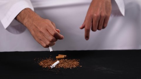 Anti-smoking to prevent its physical and psychological harms, gestures indicating caution against addiction, drug use, and harmful chemicals, stopping harmful behavioral habits, a close-up shot of the hand of a young Emirati Arab man wearing a kandura destroying cigarettes.