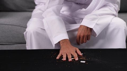 ايماءات تدل على الحذر من الإدمان، محاربة عادة التدخين، تعاطي المخدرات والمواد الكيميائية الضارة، التوقف عن اتباع العادات السلوكية الضارة، تصوير مقرب ليد شاب عربي خليجي إماراتي يرتدي الكندورة يقوم بإتلاف السجائر