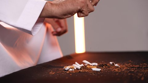 Abuse of toxic substances, stopping harmful behavioral habits, combating the smoking habit, a close-up shot of a young Arab Gulf Emirati man wearing a kandura destroying cigarettes, gestures indicating caution against addiction.