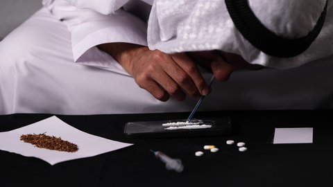 العواقب السلبية للإدمان، المعاناة من الاضطرابات النفسية والمشاكل الصحية، تعاطي المواد السامة عن طريق شمها، القيام بعادات سلوكية ضارة، تصوير مقرب لرجل عربي خليجي إماراتي يرتدي الكندورة والغترة يقوم باستنشاق المخدرات
