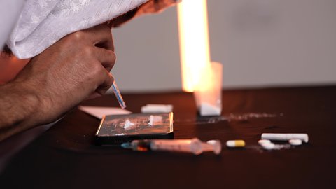 استنشاق المواد السامة، المعاناة من الاضطرابات النفسية والمشاكل الصحية، الآثار السلبية للادمان، تصوير مقرب من الجانب لرجل عربي خليجي إماراتي يرتدي الكندورة والغترة يقوم باستنشاق المخدرات