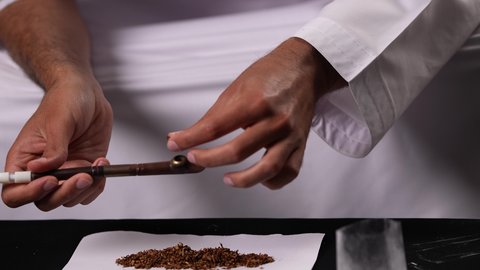 The health and psychological risks resulting from addiction to tobacco and drugs, suffering from psychological disorders and health problems, engaging in harmful behavioral habits and consuming toxic substances, a close-up shot of the hand of an Emirati Arab man lighting a cigarette butt.